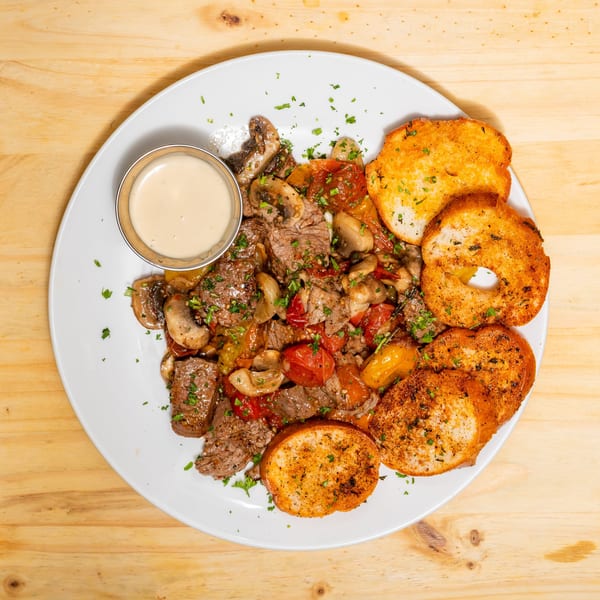 Steak and mushroom stir-fry with tomatoes, bell peppers, and garlic bread on a white plate.